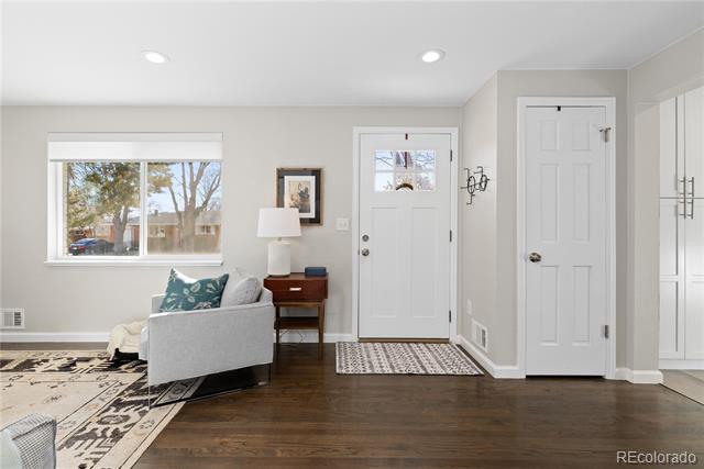 Home entry with white doors, a window overlooking trees, dark wood floors, and a gray armchair.