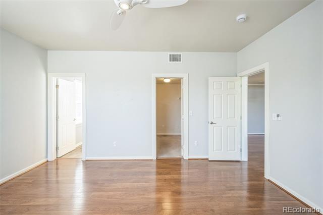 Empty room with hardwood floors, a ceiling fan, and three open doorways.