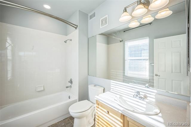 Bathroom with a white tub, toilet, and wood vanity beneath a large mirror.