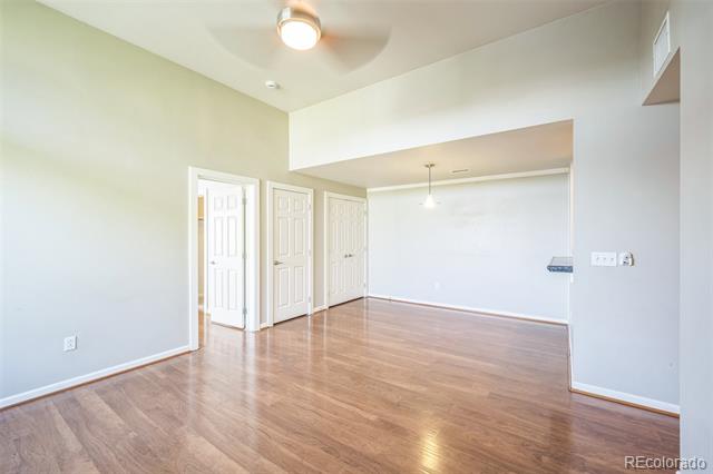 Empty room with glossy wood floors and high ceiling, opening into an adjoining space.
