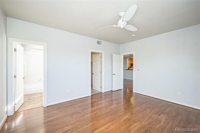 Empty room with wood flooring, a ceiling fan, and open doors to a bathroom and hallway.
