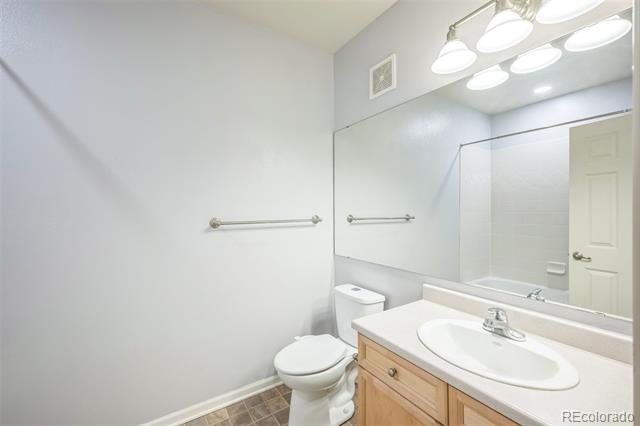 Bathroom with a wood vanity and oval sink, large mirror, toilet, and brown tile floor.
