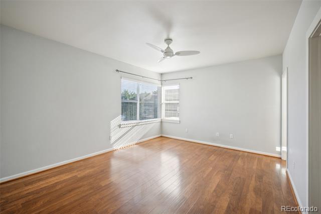 Vacant bedroom with hardwood floors, corner windows, and a ceiling fan.