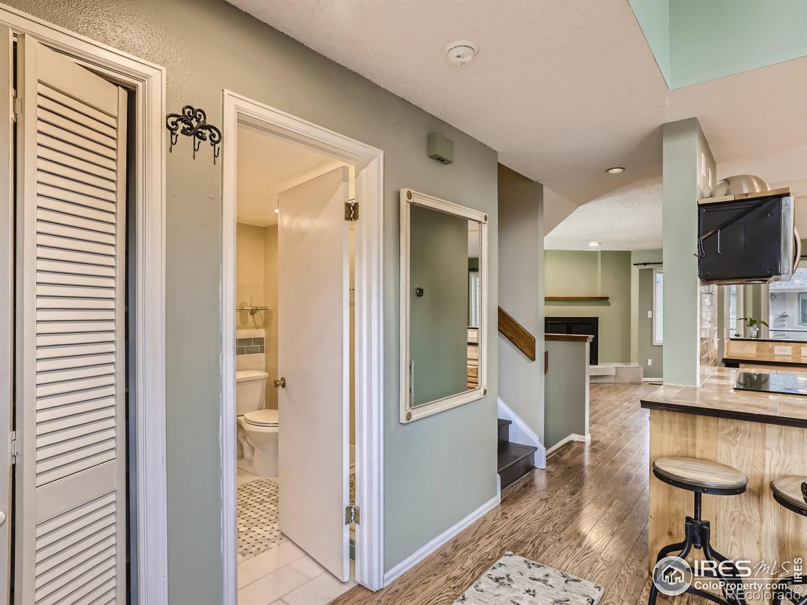 Condo hallway with wood floors, an open bathroom door, and a kitchen island with bar stools.