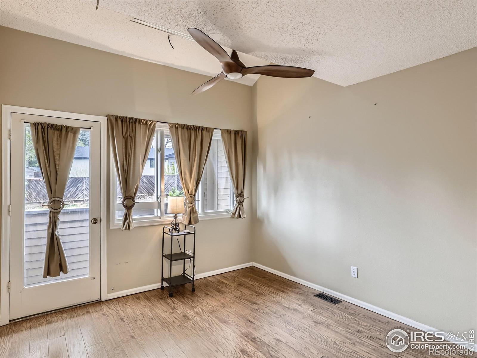 Empty room with a ceiling fan, wood-look flooring, and curtained windows beside a glass patio door.