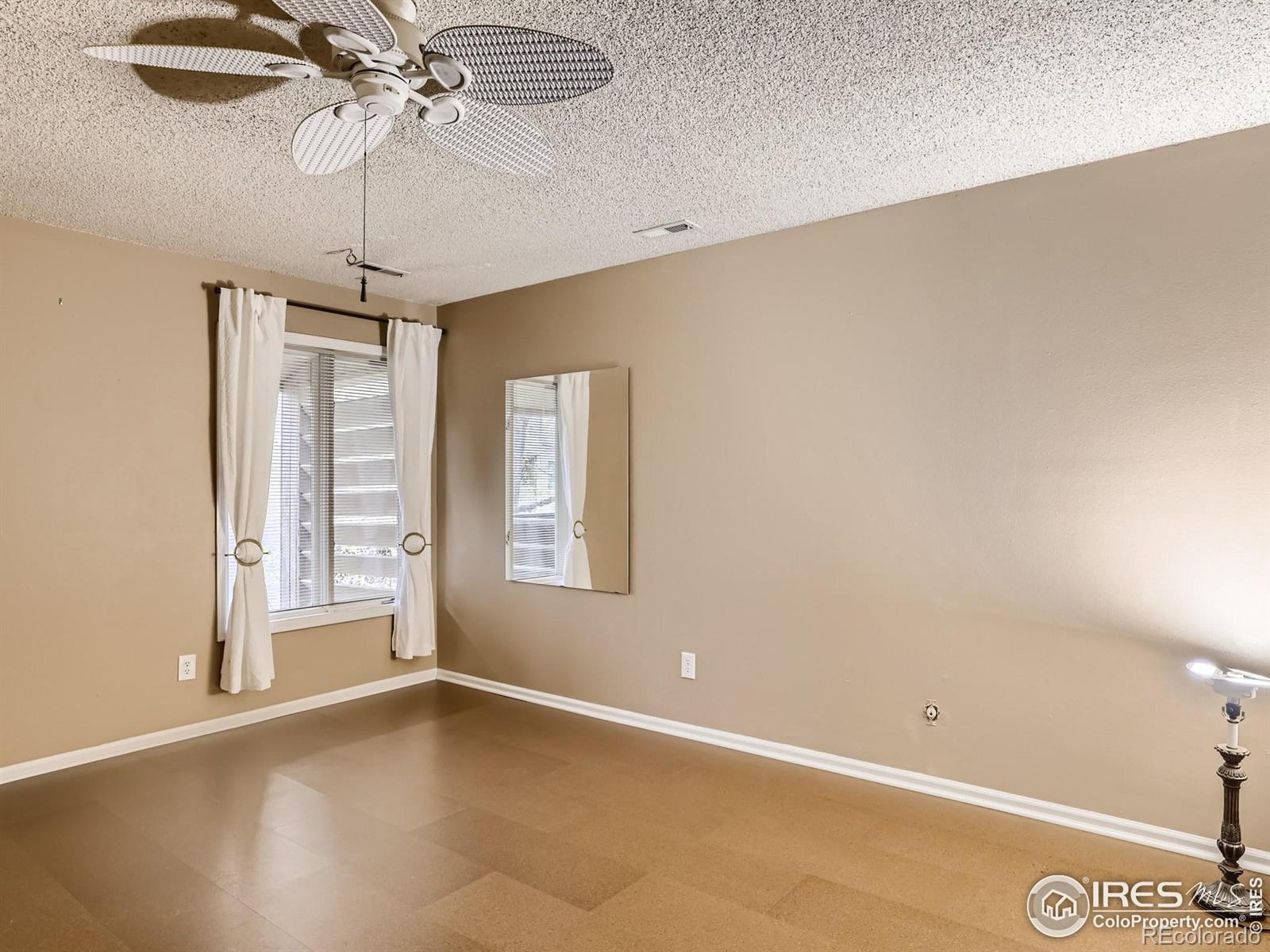 Empty condo room with beige walls, tiled floor, curtained window, and ceiling fan.