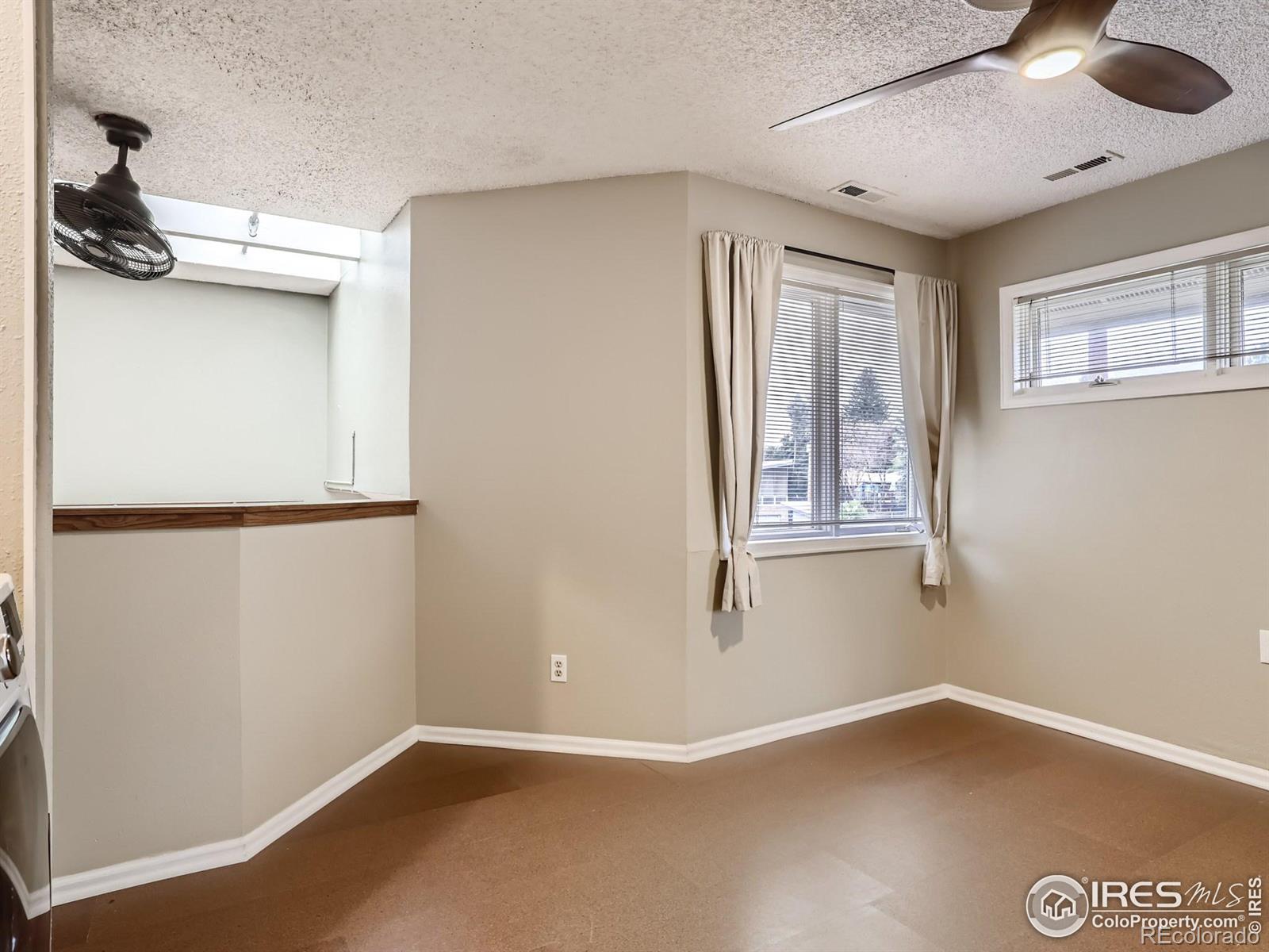 Empty carpeted room with two windows, ceiling fans, and a wood-trimmed pass-through.