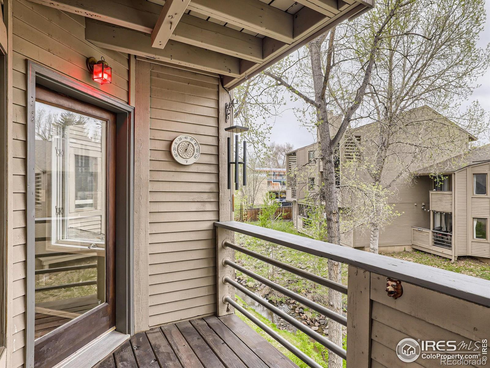 Covered wooden condo balcony overlooking leafy trees, neighboring homes, and a small creek.