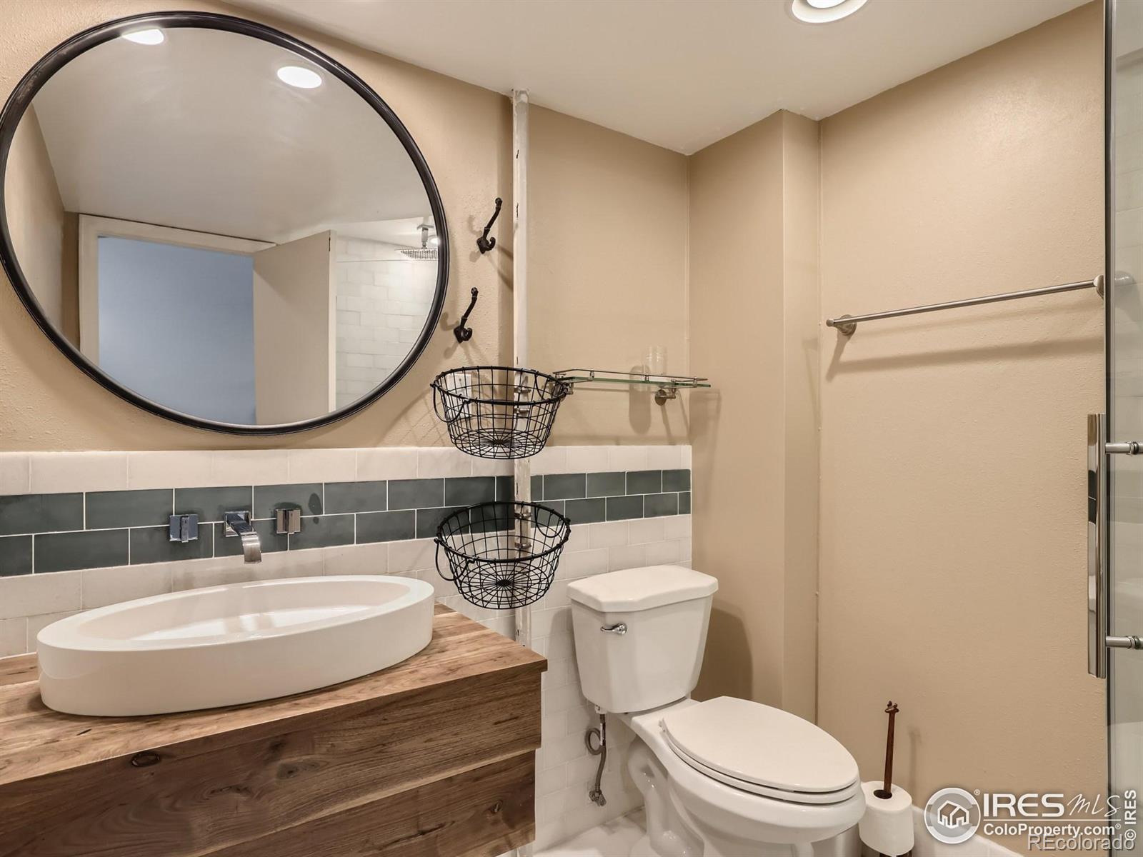 Bathroom with a wood vanity, vessel sink, round mirror, and glass-enclosed shower.