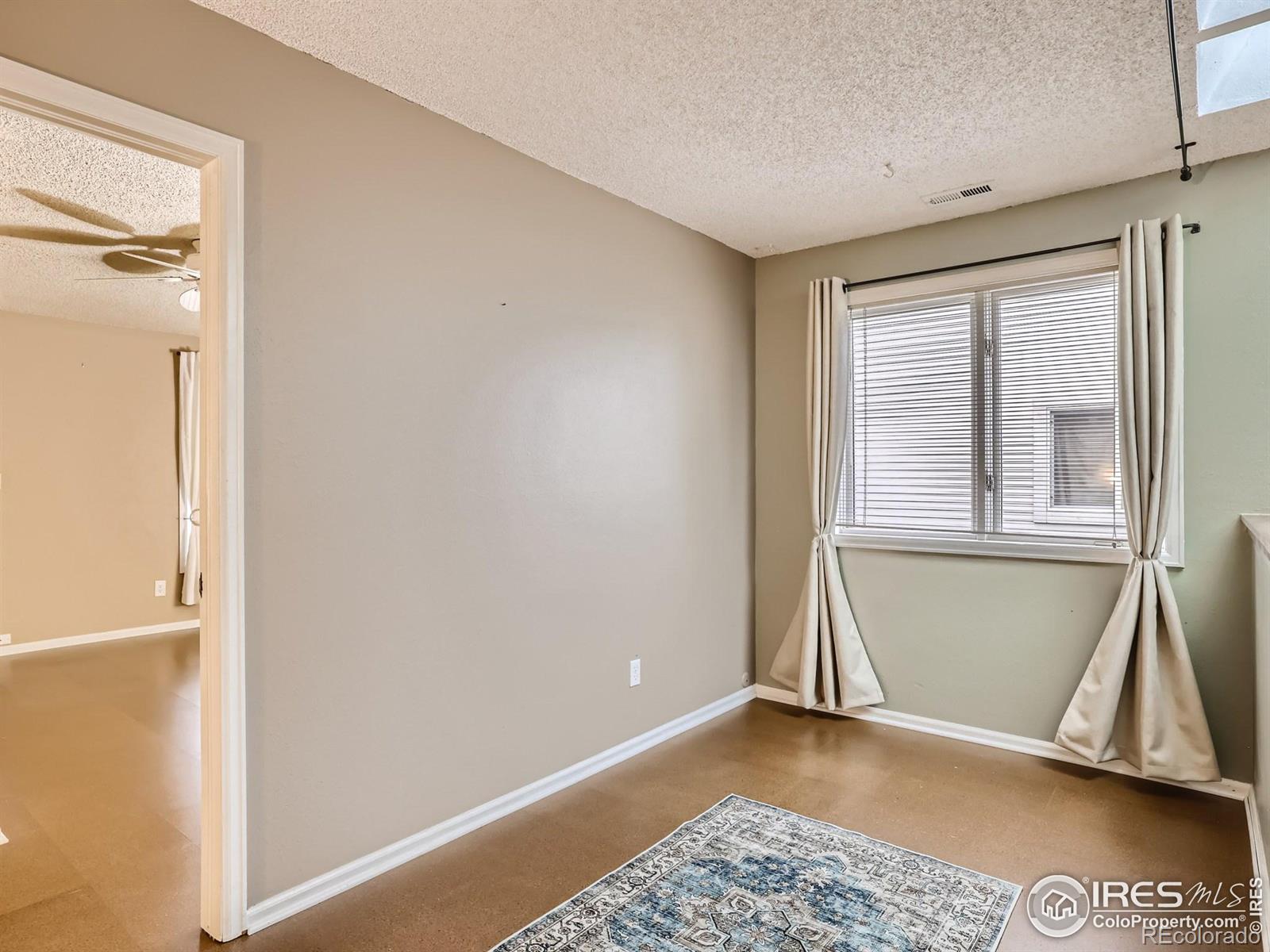 Empty bedroom with a curtained window, blinds, and a patterned rug.