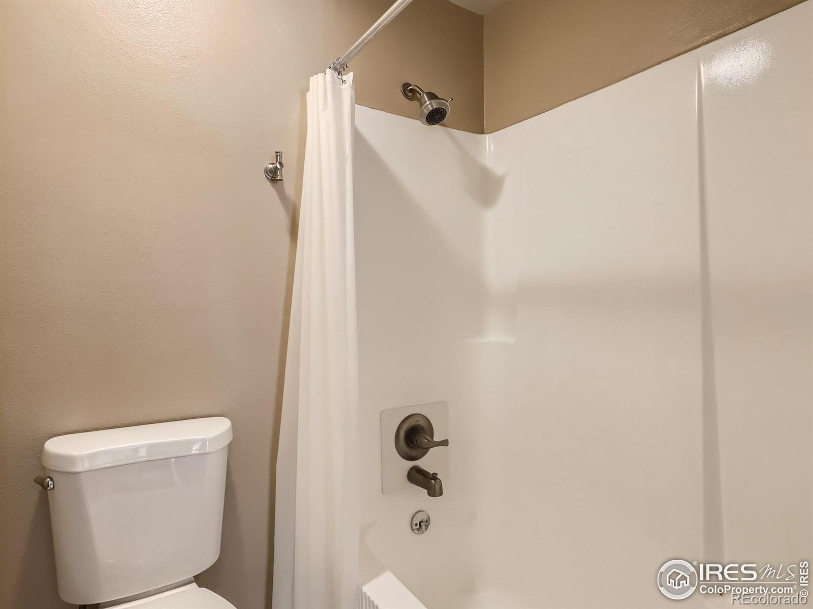 Bathroom with a white tub and shower, curtain, chrome fixtures, and toilet.