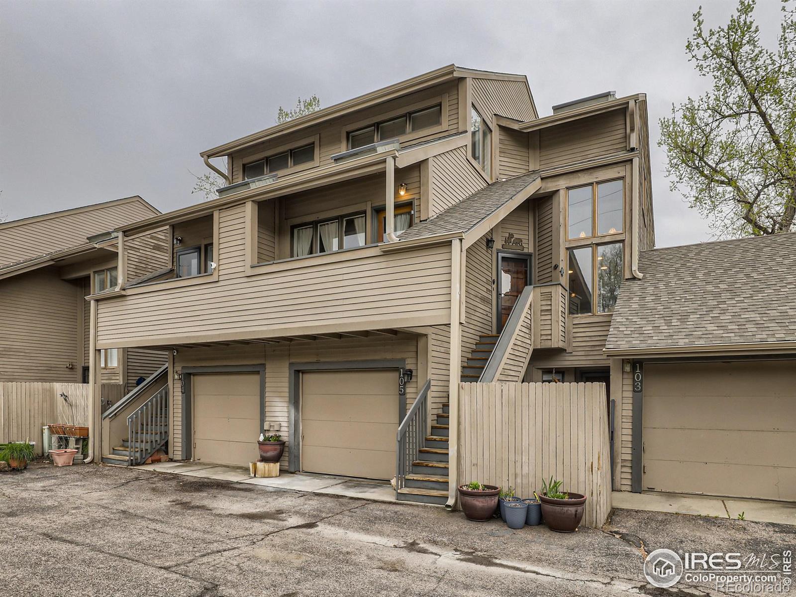 Tan multi-level condo with a covered balcony, exterior stairs, and attached garages.