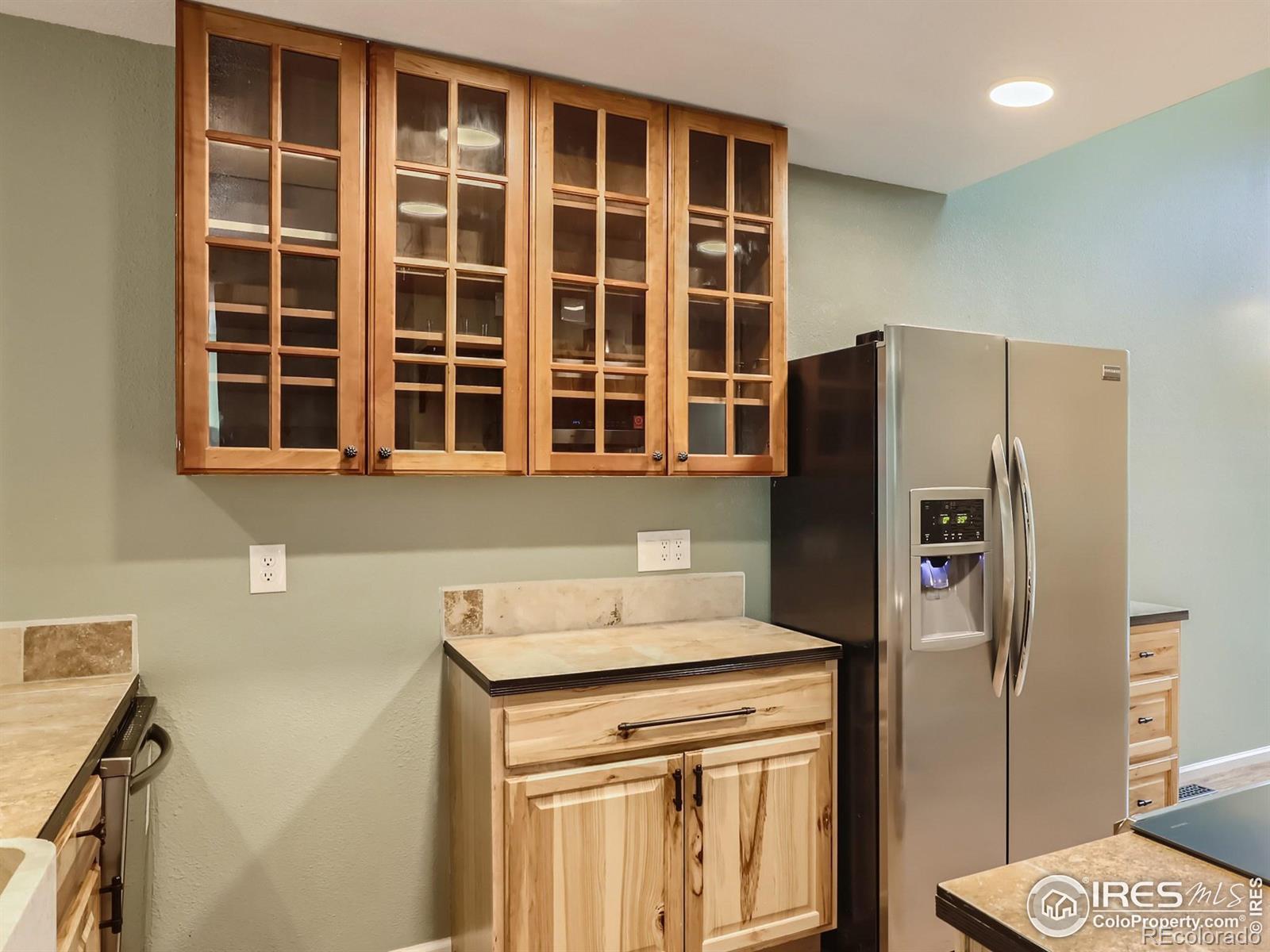 Kitchen with glass-front wood cabinets, stone countertops, and a stainless-steel refrigerator.
