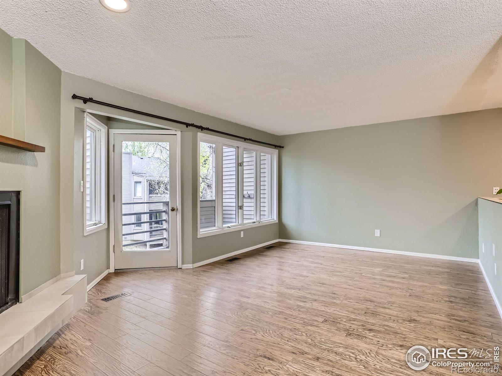 Empty living room with wood-look floors, a corner fireplace, and a glass patio door beside windows.
