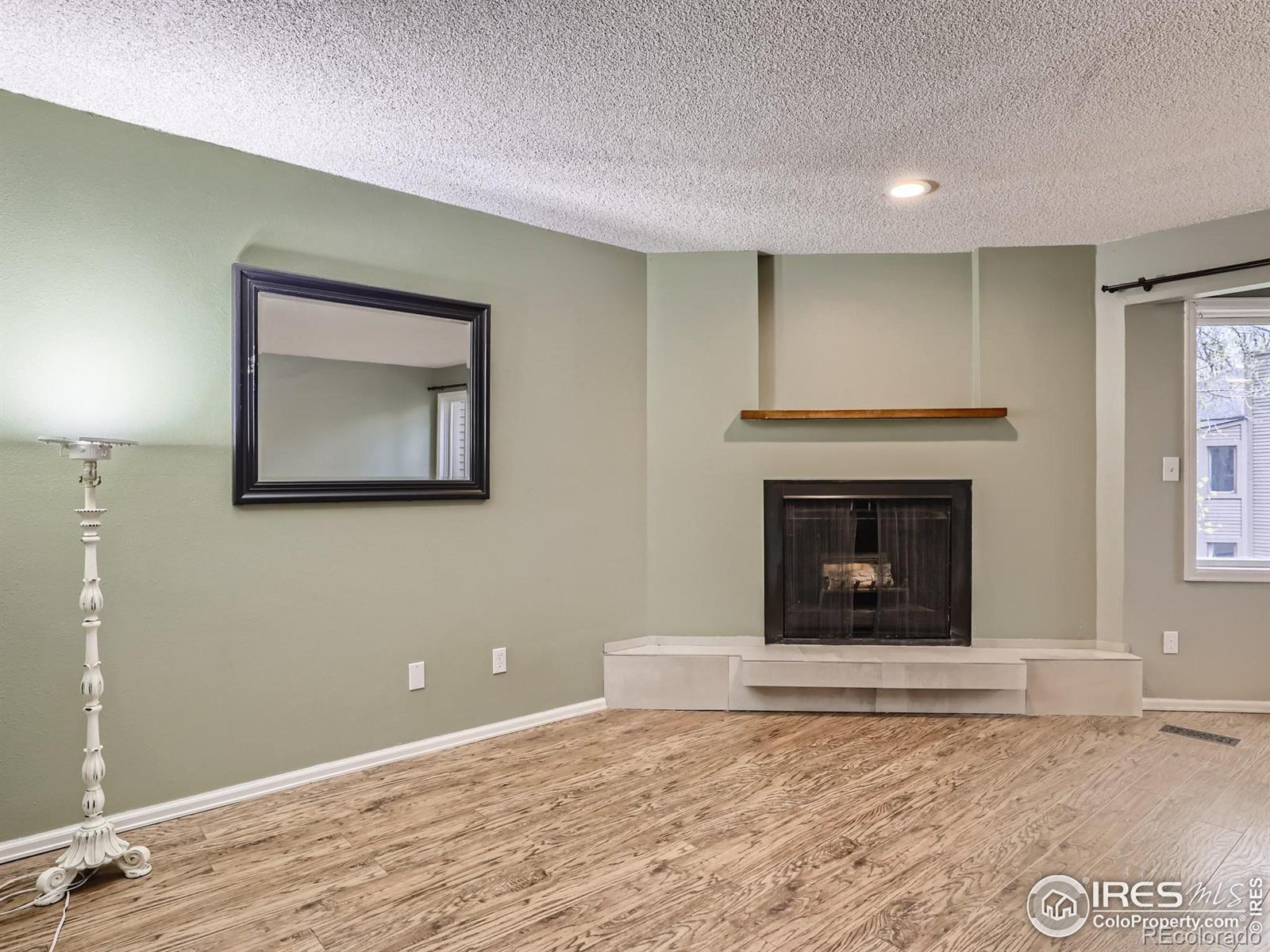 Vacant living room with a corner fireplace, raised hearth, wood floors, and large framed mirror.