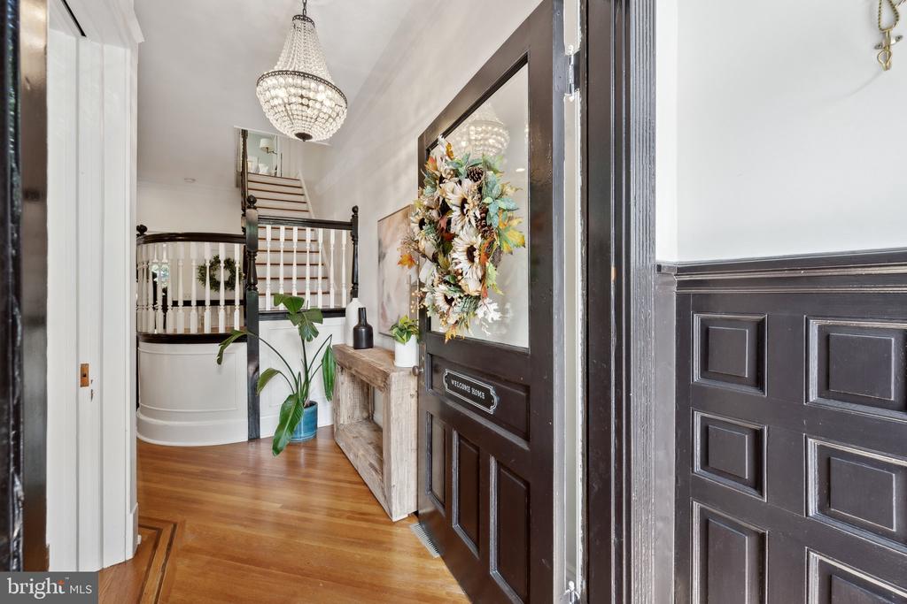 Entry foyer with curved staircase, crystal chandelier, hardwood floors, and a dark paneled front door.