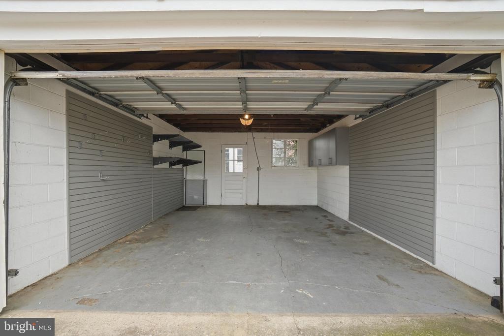 Empty garage with a concrete floor, gray wall panels, and storage shelves along the sides.