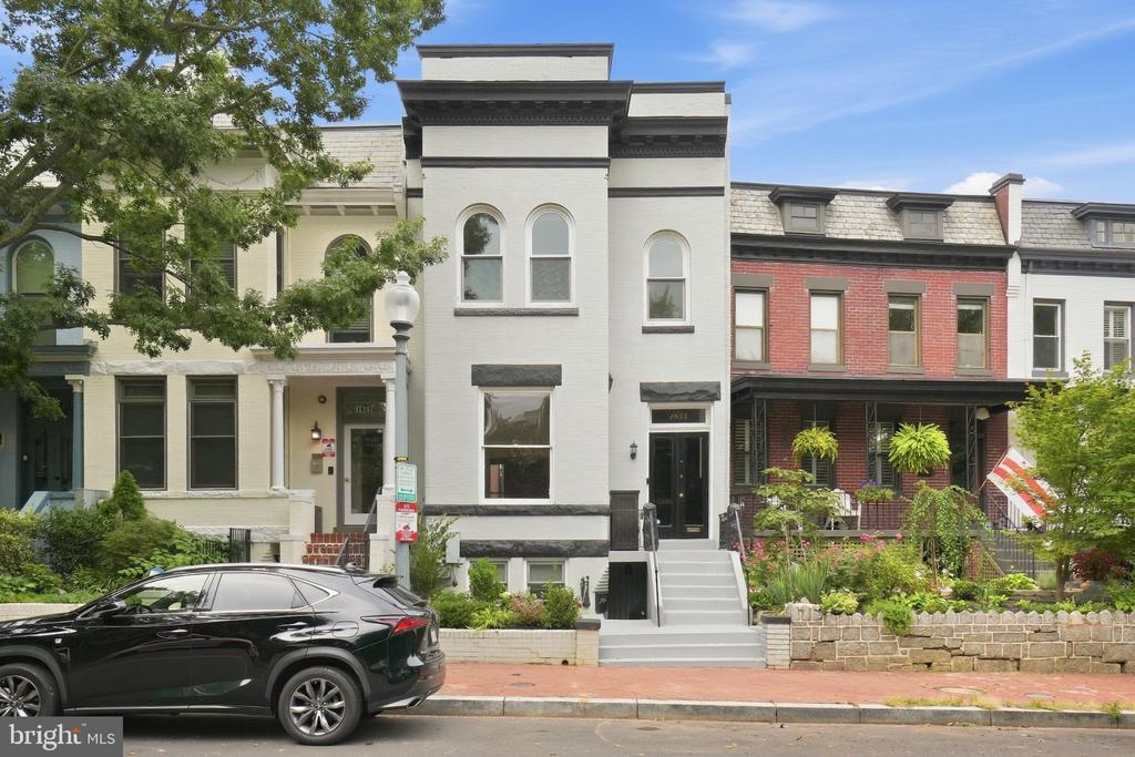 White brick row house with arched windows, dark trim, front steps, and landscaped beds.