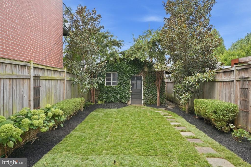 Enclosed backyard with a stepping-stone path, ivy-covered rear wall, wooden fences, and mature trees.