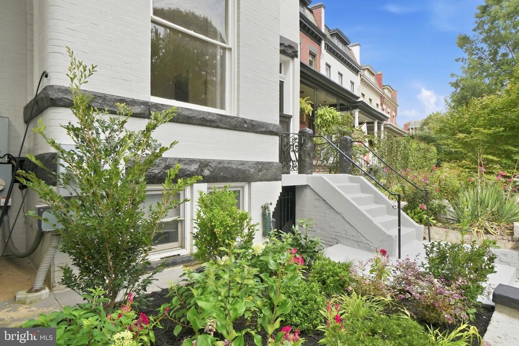 White brick rowhouse with dark stone trim, front steps, and a lush garden.
