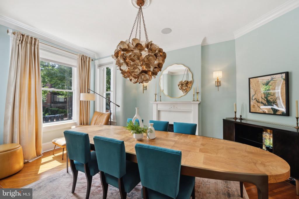 Dining room with a large wood table, teal chairs, tall windows, and a decorative chandelier.