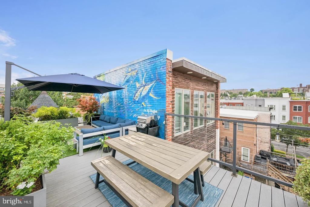 Rooftop terrace with a wood dining set, blue lounge seating, grill, and mural wall.