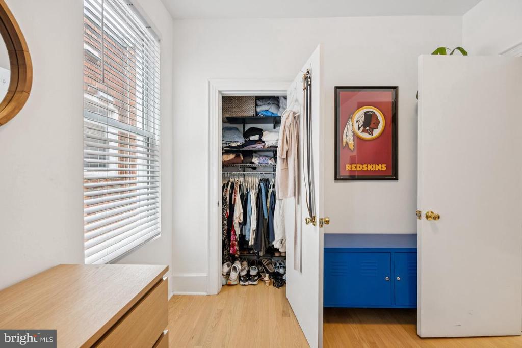 Walk-in closet with hanging clothes, shoes, window blinds, and blue built-in cabinets.