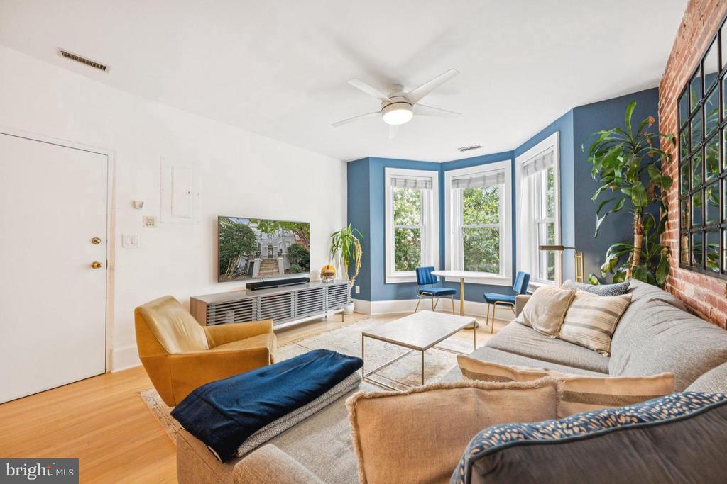 Living room with blue bay-window walls, exposed brick, and a furnished seating area.