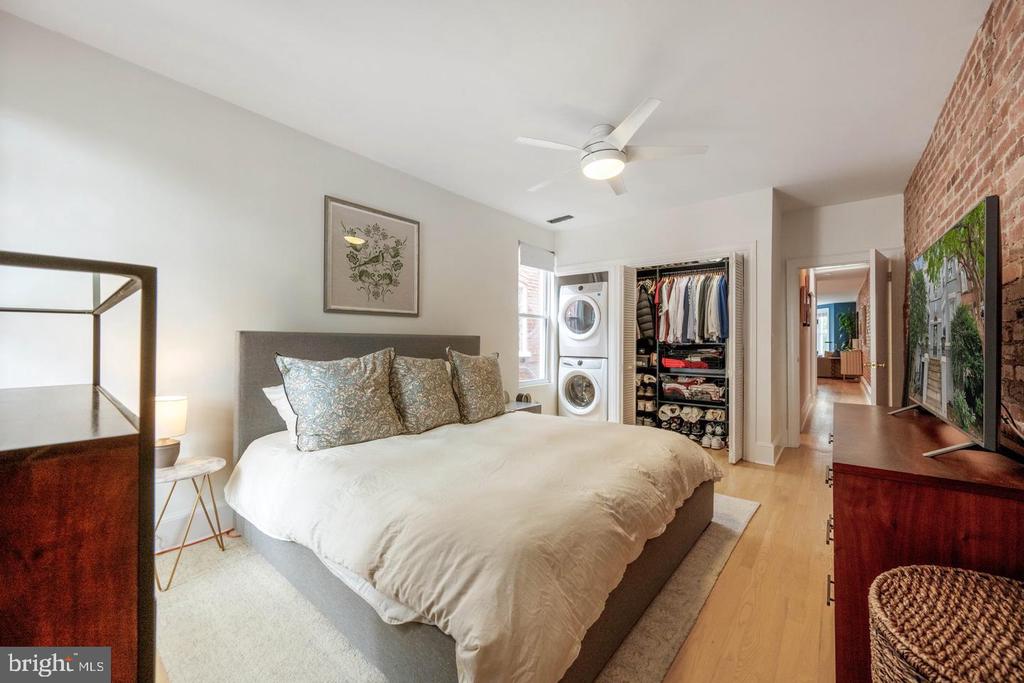 Furnished bedroom with a large bed, open clothes closet, and stacked washer and dryer.