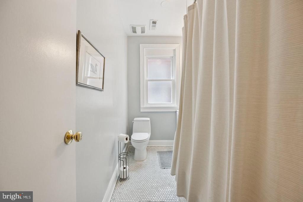 Bathroom with a white toilet beneath a window, cream shower curtain, and hexagonal mosaic tile floor.