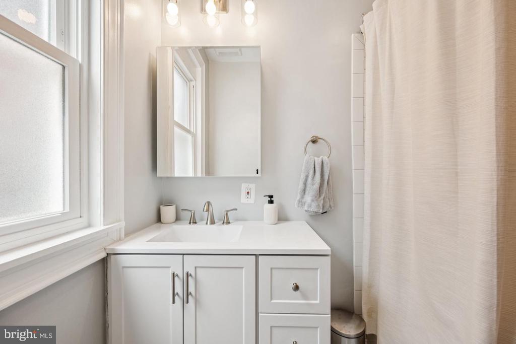 Bathroom with a white paneled vanity, large mirror, frosted window, and light shower curtain.