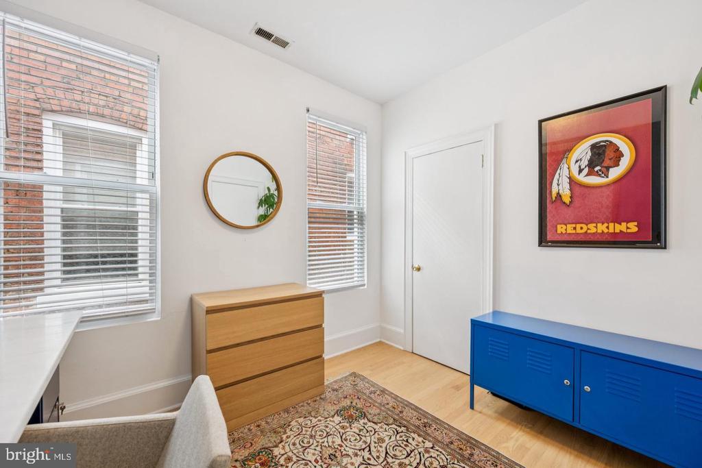 Furnished room with two blind-covered windows, a wood dresser, blue cabinet, and framed Redskins print.
