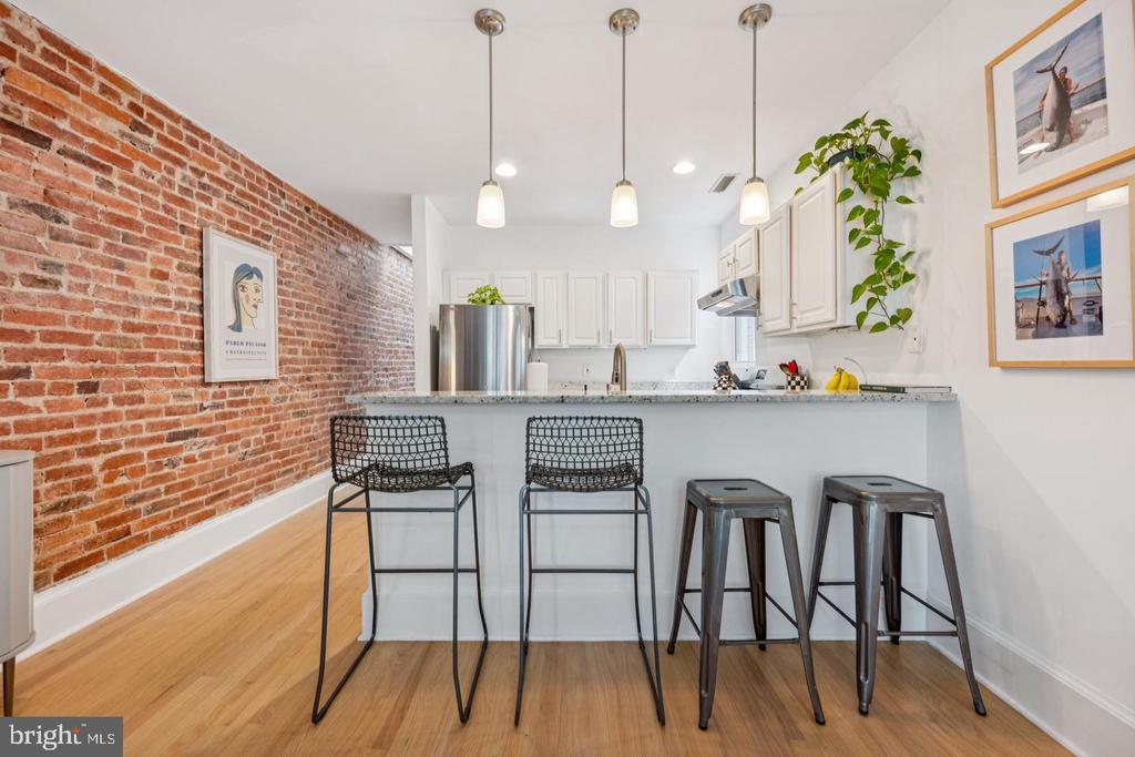 Kitchen with an exposed brick wall, white cabinetry, and a breakfast bar with seating.
