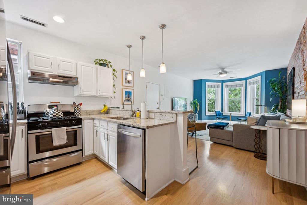 Open kitchen and living room with granite counters, stainless appliances, blue bay-window wall, and hardwood floors.
