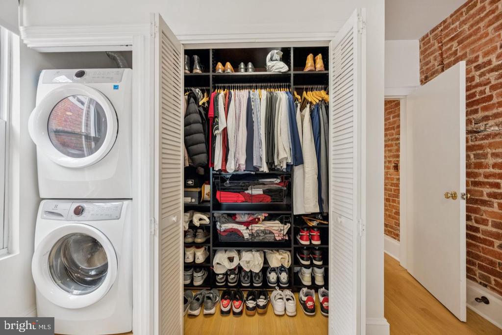 Organized walk-in closet with clothing and shoe shelves beside a stacked washer and dryer.