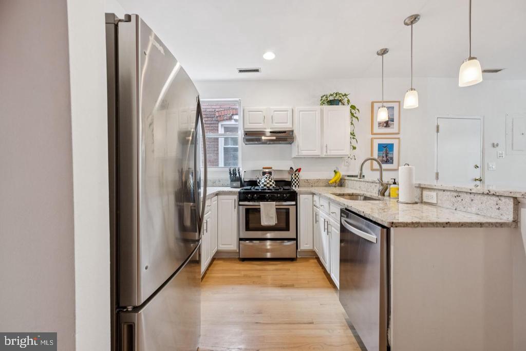 Modern kitchen with white cabinets, granite counters, stainless steel appliances, and light wood flooring.