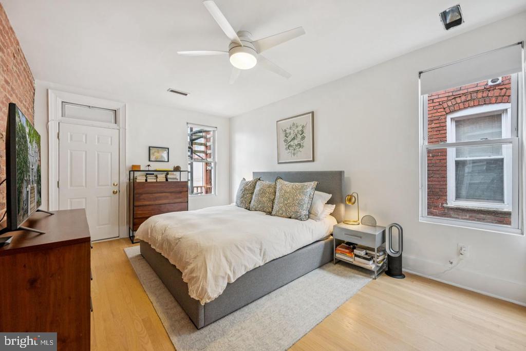 Bedroom with a king-size bed, ceiling fan, and windows facing a brick wall.