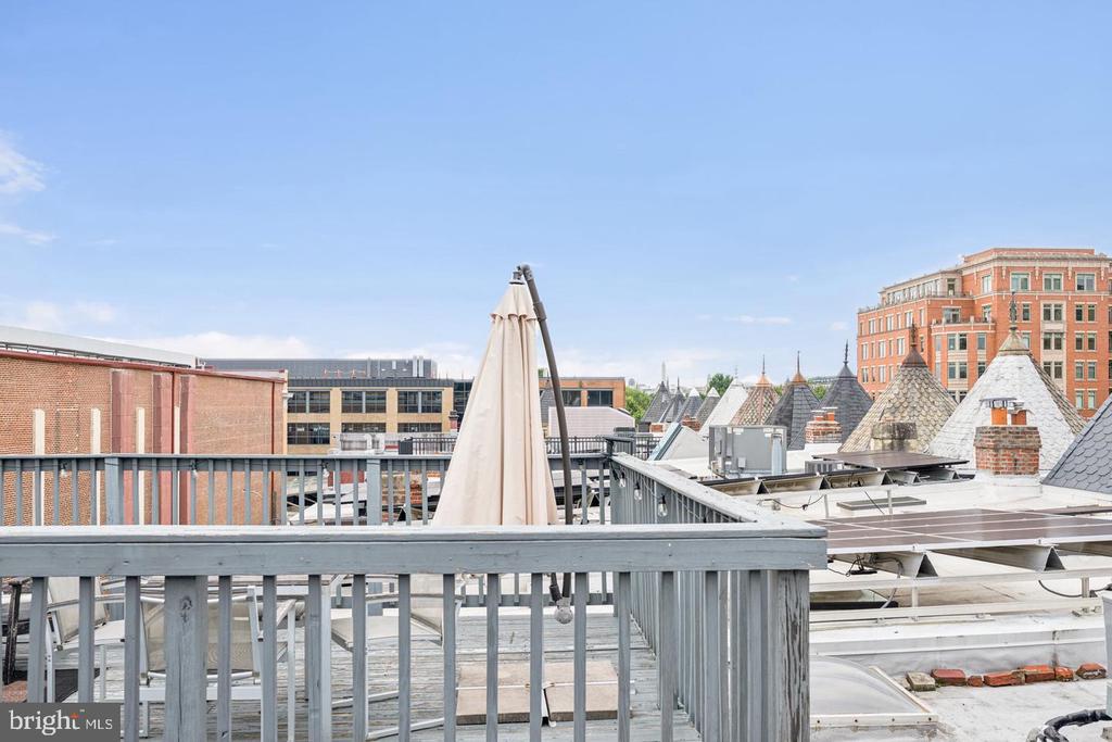 Rooftop deck with a closed umbrella and views of nearby city buildings.