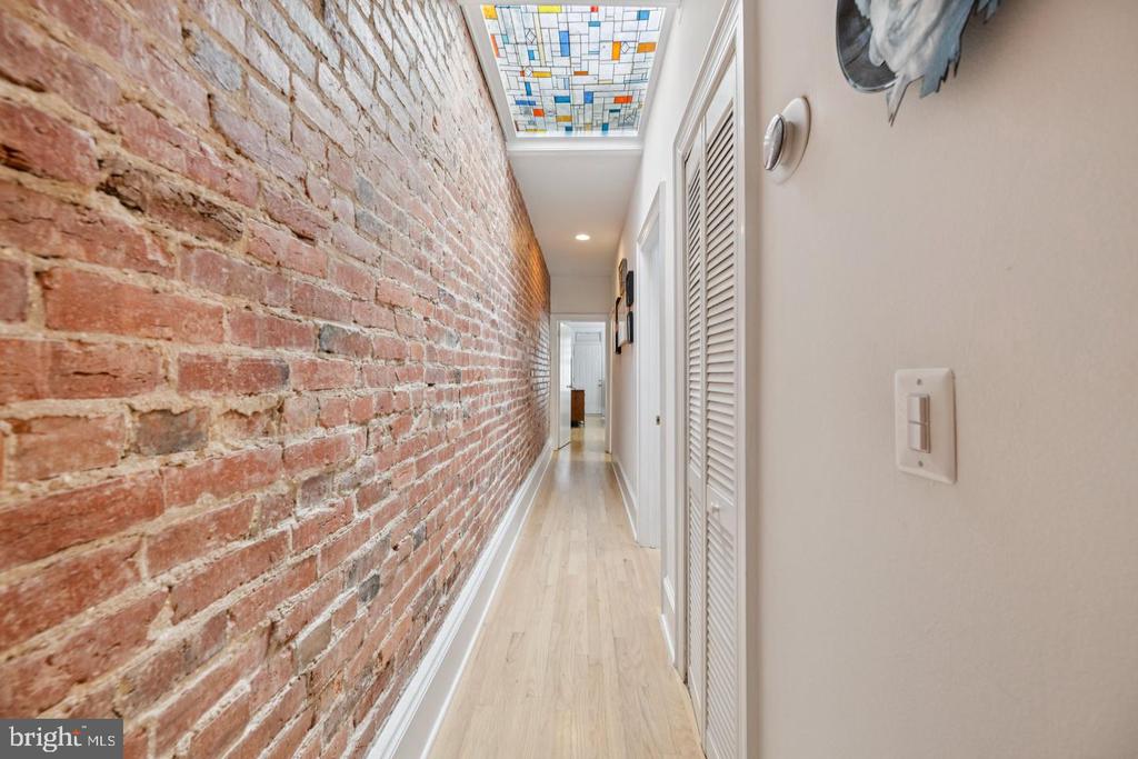 Hallway with an exposed brick wall, pale wood flooring, and a stained-glass ceiling panel.