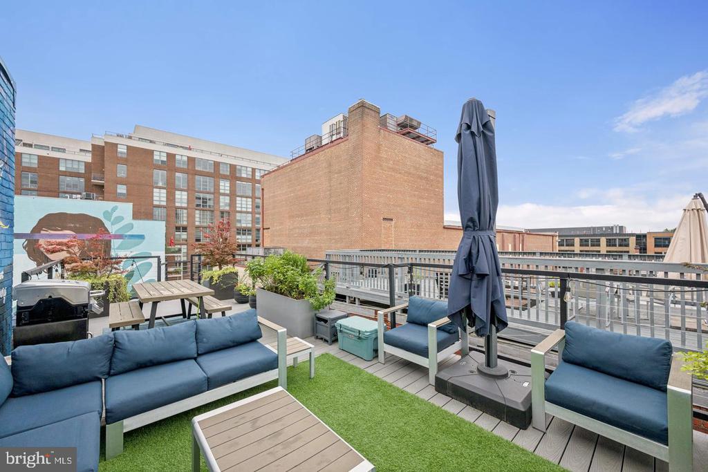 Furnished rooftop deck with blue lounge seating and planters overlooking nearby city buildings.