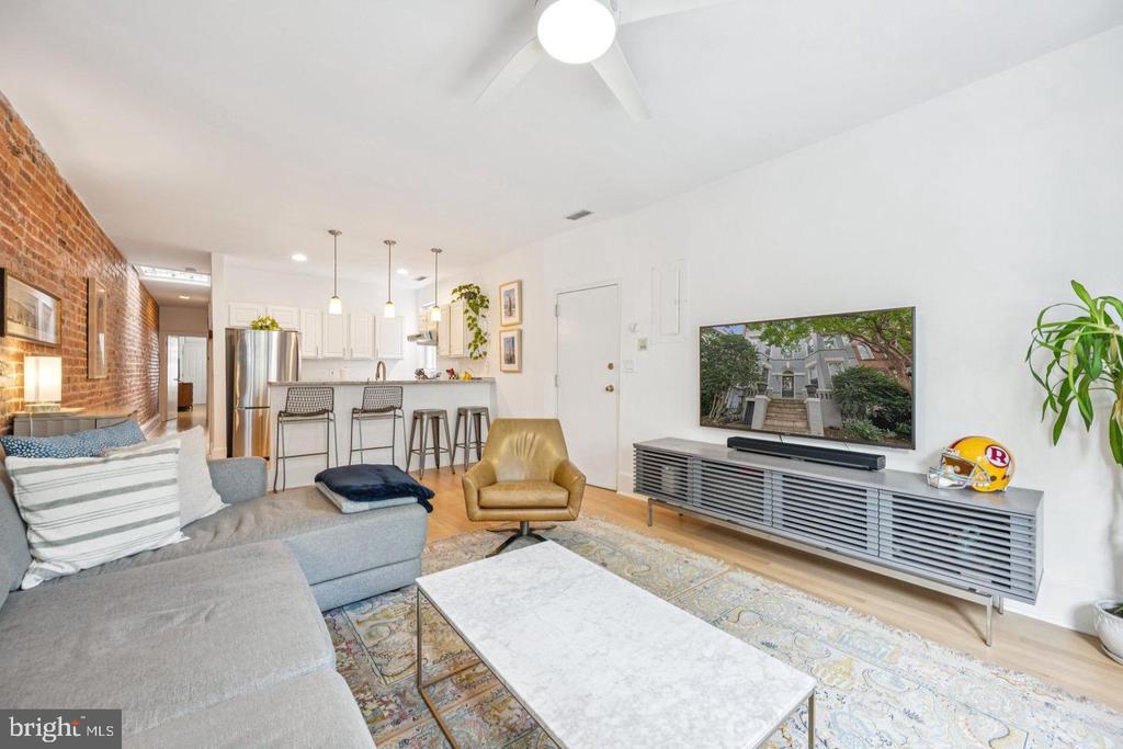 Living room with an exposed brick wall, gray sectional, and open kitchen with breakfast bar.