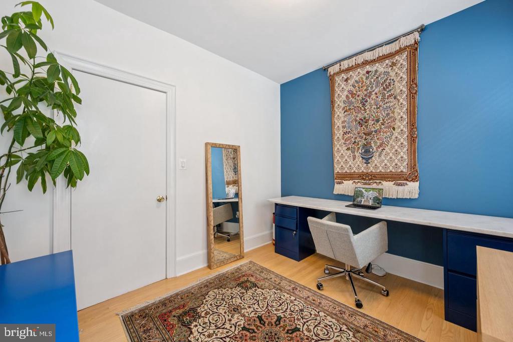 Home office with a built-in navy desk, blue accent wall, ornate tapestry, and patterned rug.