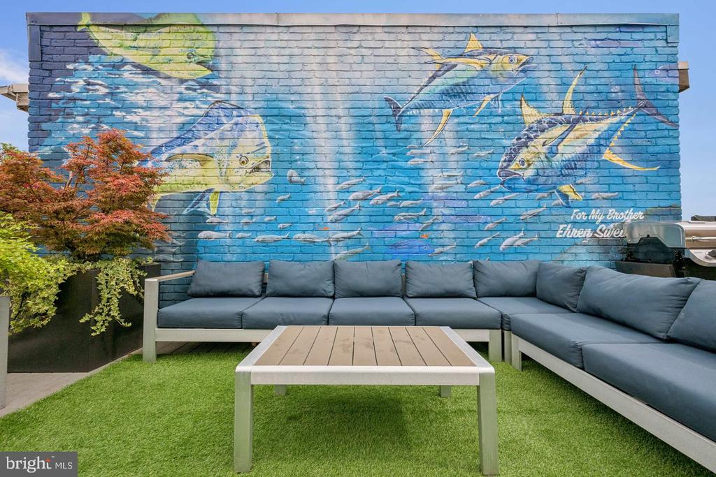 Outdoor patio with a blue fish mural, gray sectional seating, and artificial turf.
