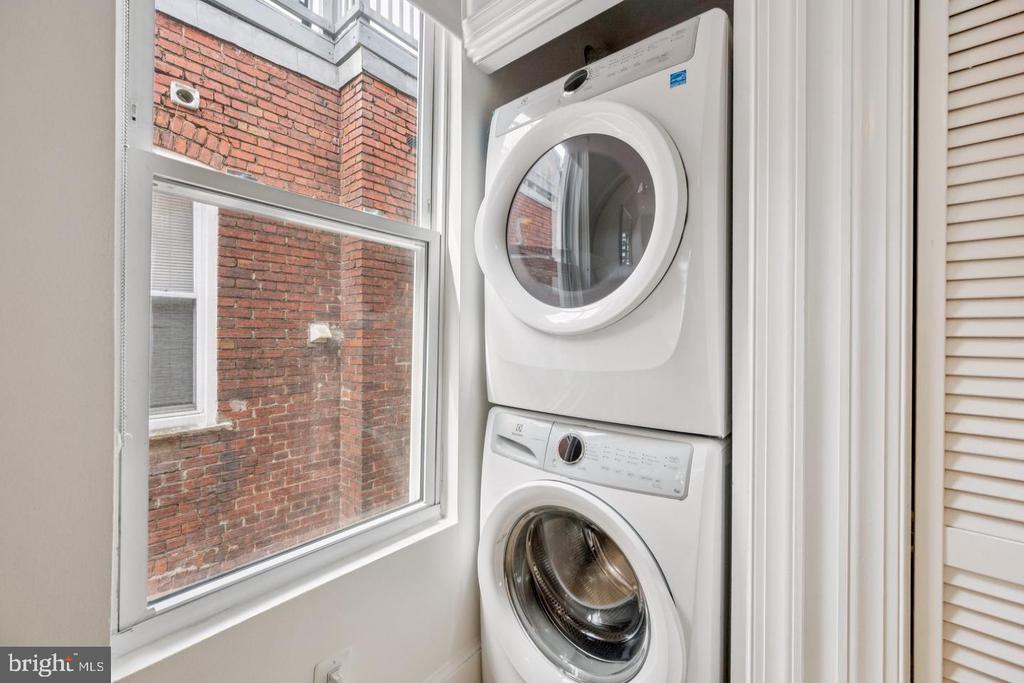 Stacked washer and dryer beside a large window overlooking a brick wall.