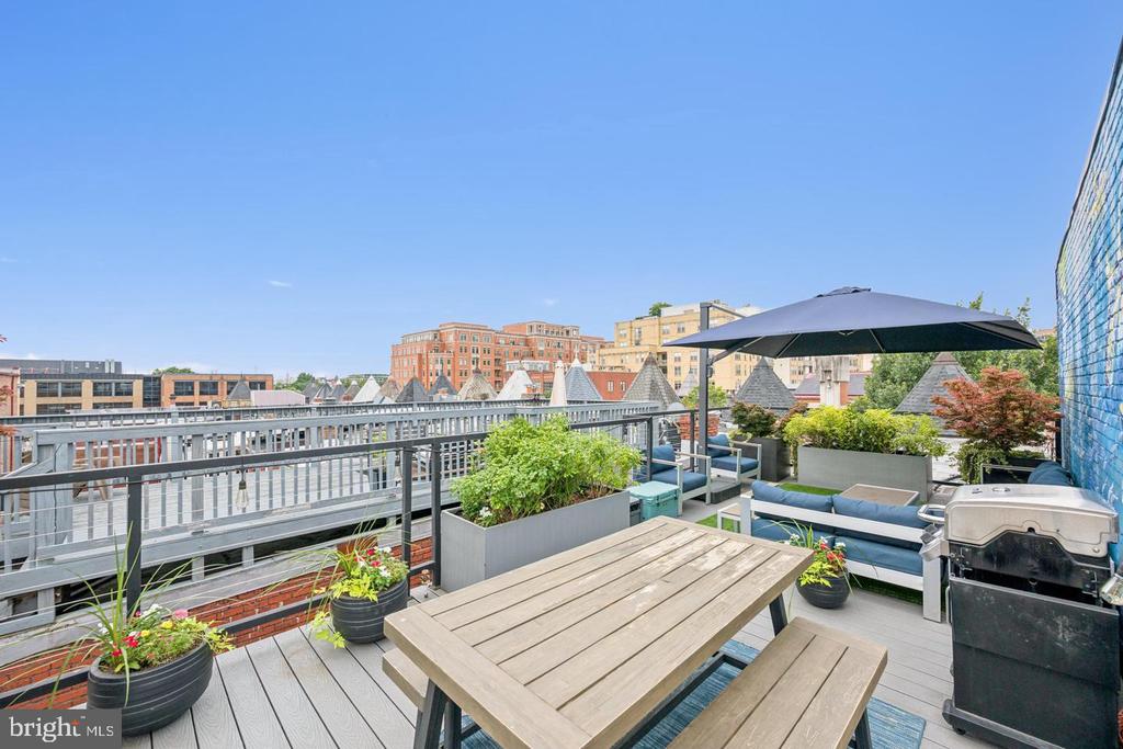 Rooftop deck with wooden dining set, umbrella-shaded lounge seating, planters, and city views.