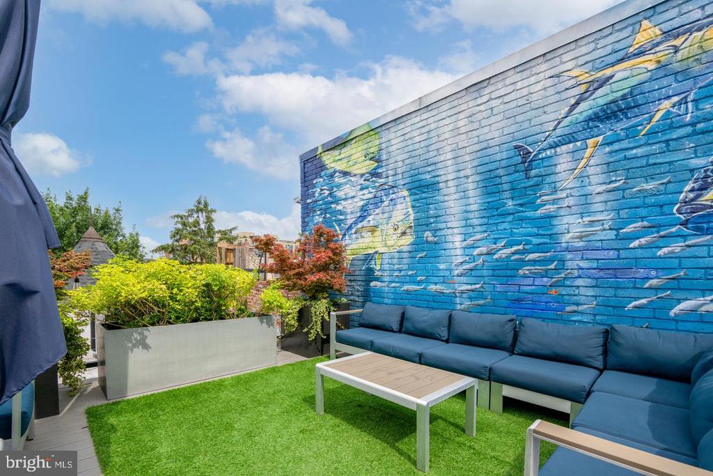 Rooftop patio with blue seating, artificial turf, greenery, and a large blue mural.