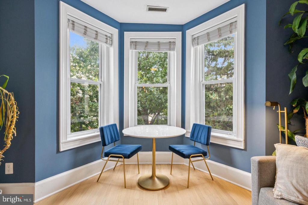 Dining nook with a round table and blue chairs beside three large bay windows.
