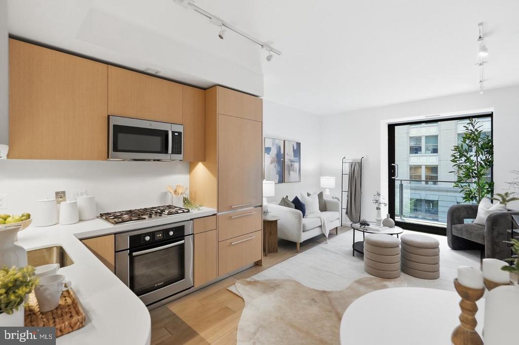 Open-plan kitchen and living room with light wood cabinetry and a large window.