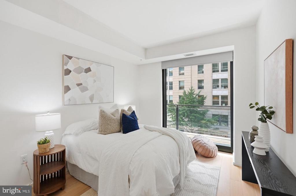 Bright bedroom with white bedding, a large window, and nearby buildings visible outside.