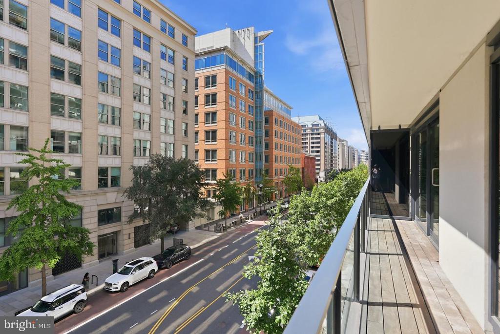 Apartment balcony overlooking a tree-lined urban street and modern buildings.